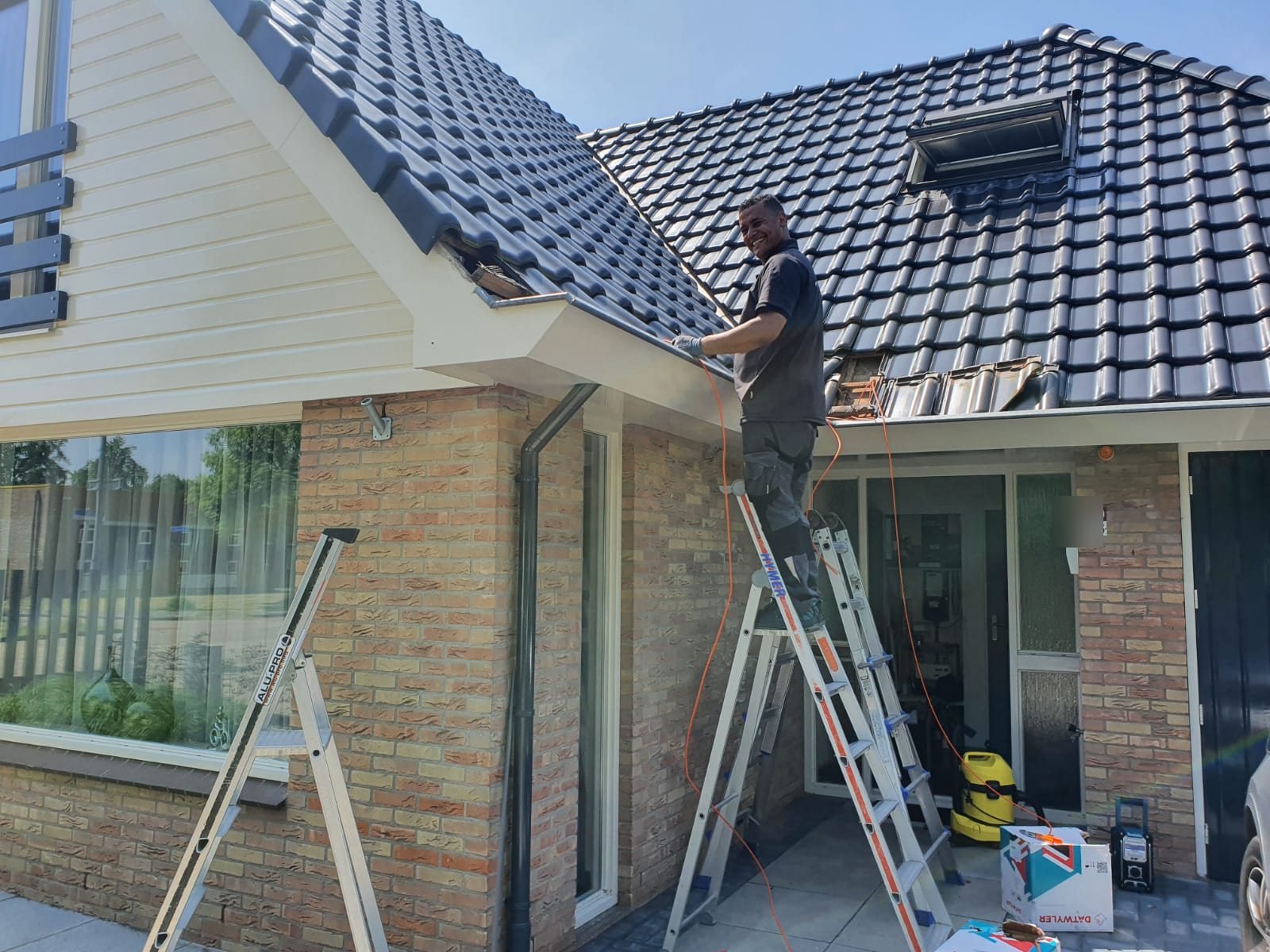 Lachende monteur op een trap legt een kabel langs de dakgoot van een woning