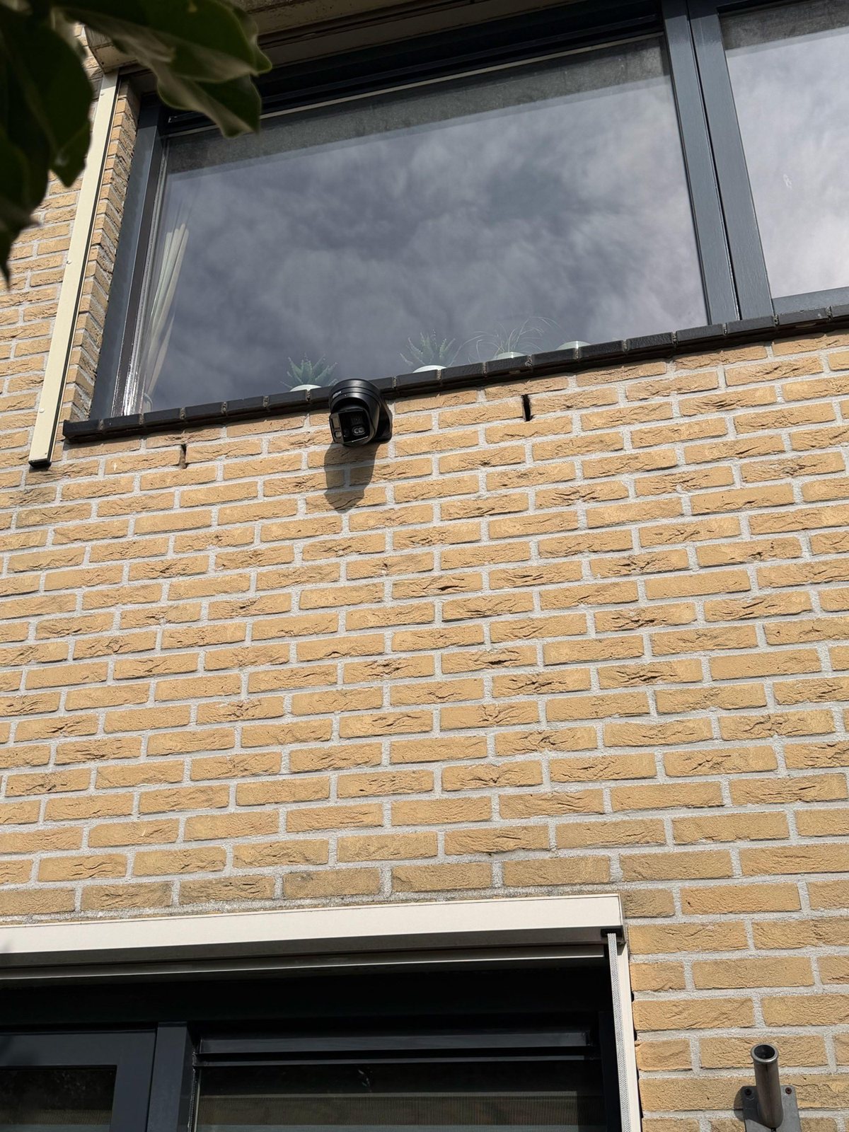Zwarte 180-gradencamera aan een bakstenen voorgevel, onder een raam