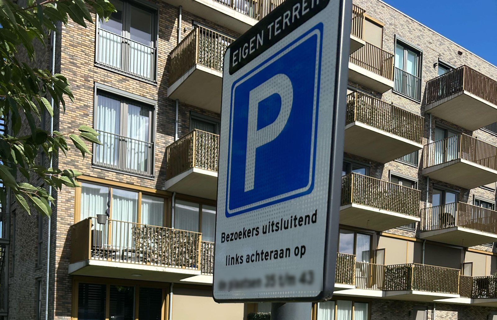 Parkeerterrein van een appartementencomplex met een parkeerbord op eigen terrein